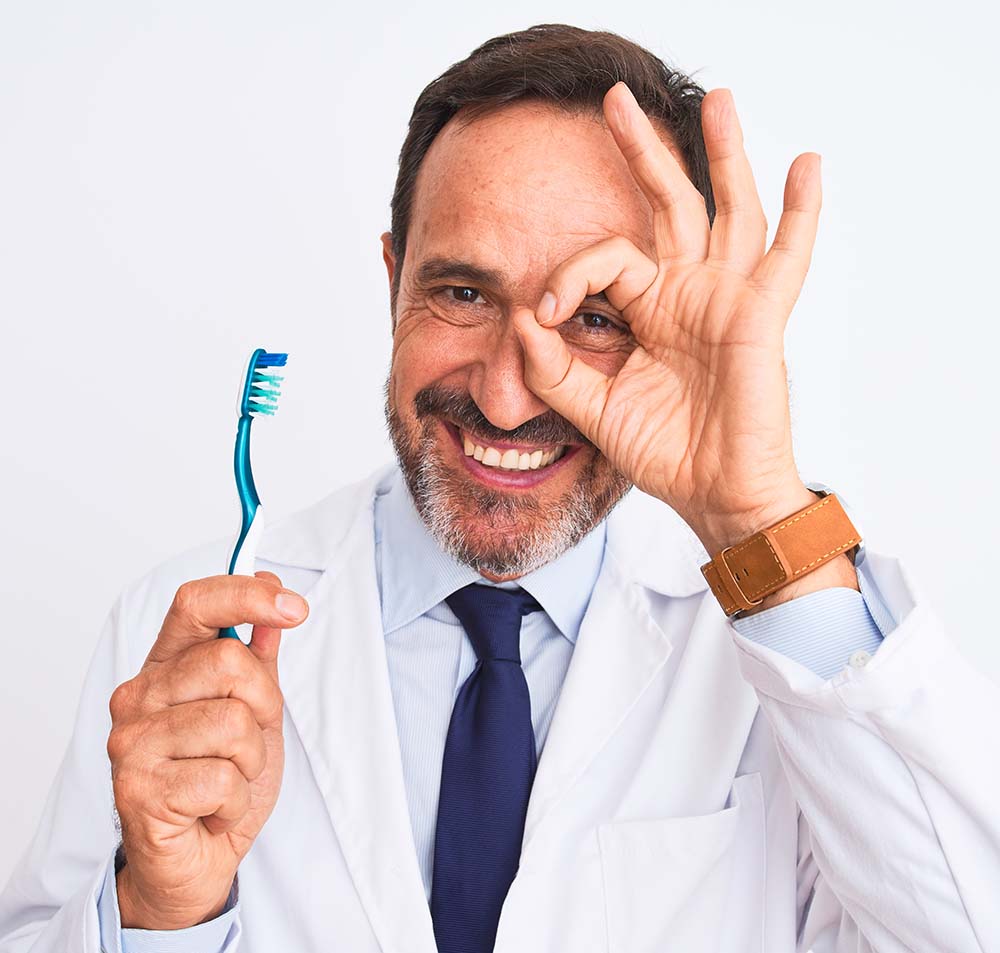 Middle age dentist man holding toothbrush standing over isolated white background with happy face smiling doing ok sign with hand on eye looking through fingers
